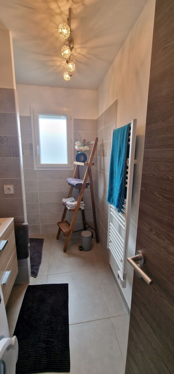 A compact bathroom with a shower, a towel rack, a wooden ladder, and a radiator.