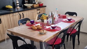 A dining table set with plates, bowls, and bottles, surrounded by chairs. - Villa Moderne Avec Jardin à 300 m du Bord de mer (Santa-Lucia-di-Moriani)