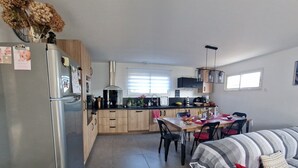 A modern kitchen with wooden cabinets, a stainless steel refrigerator, and a dining area with a table and chairs. - Villa Moderne Avec Jardin à 300 m du Bord de mer (Santa-Lucia-di-Moriani)