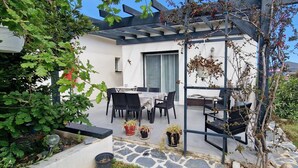 A patio with a table and chairs, surrounded by greenery and a pergola structure. - Villa Moderne Avec Jardin à 300 m du Bord de mer (Santa-Lucia-di-Moriani)
