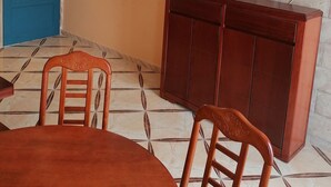 A dining area with a round table and chairs, a television mounted on a stone wall, and a blue door. - Bouzedjar-mer (Bou Zadjar)