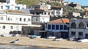 A coastal town with white buildings, a rocky shoreline, and boats docked along the beach. - Bouzedjar-mer (Bou Zadjar)