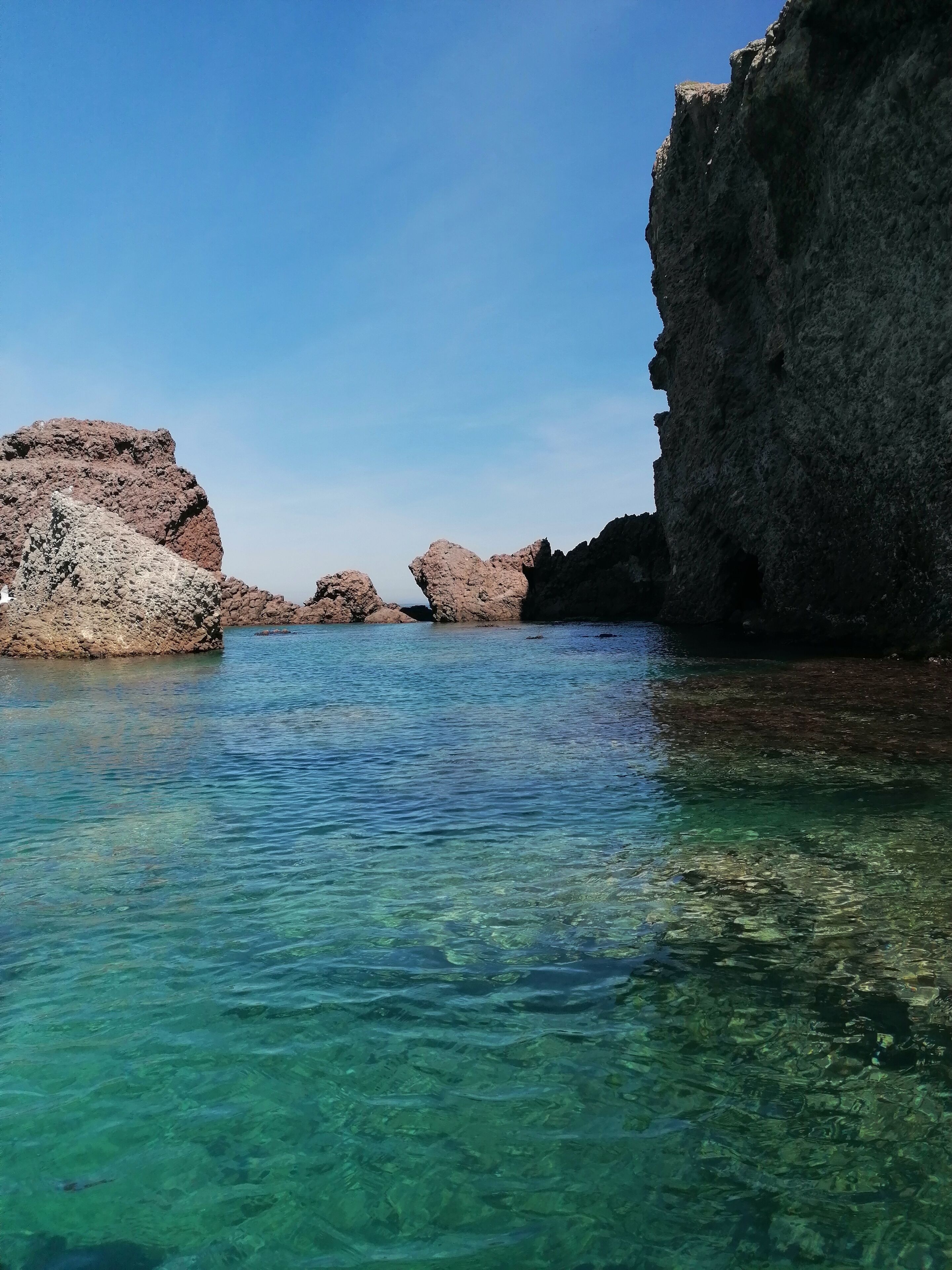 A coastal scene with clear turquoise water, rocky formations, and a large cliff.