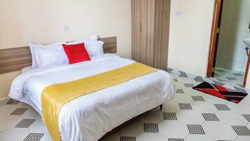 Habitación de hotel con una cama, una manta amarilla, una almohada roja y un suelo con estampado geométrico.