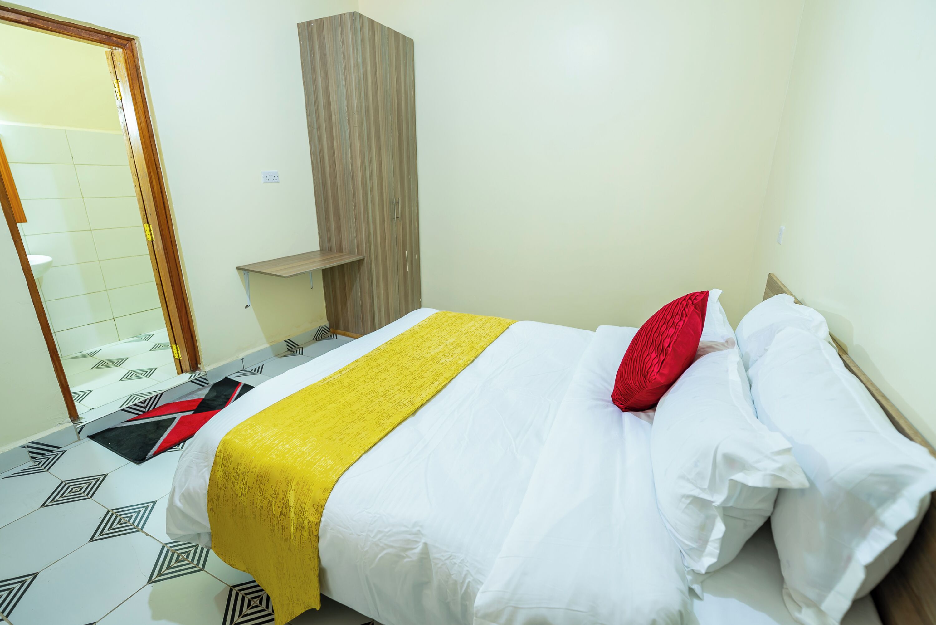 Una habitación de hotel con una cama, un armario de madera, un espejo y un suelo con diseño.