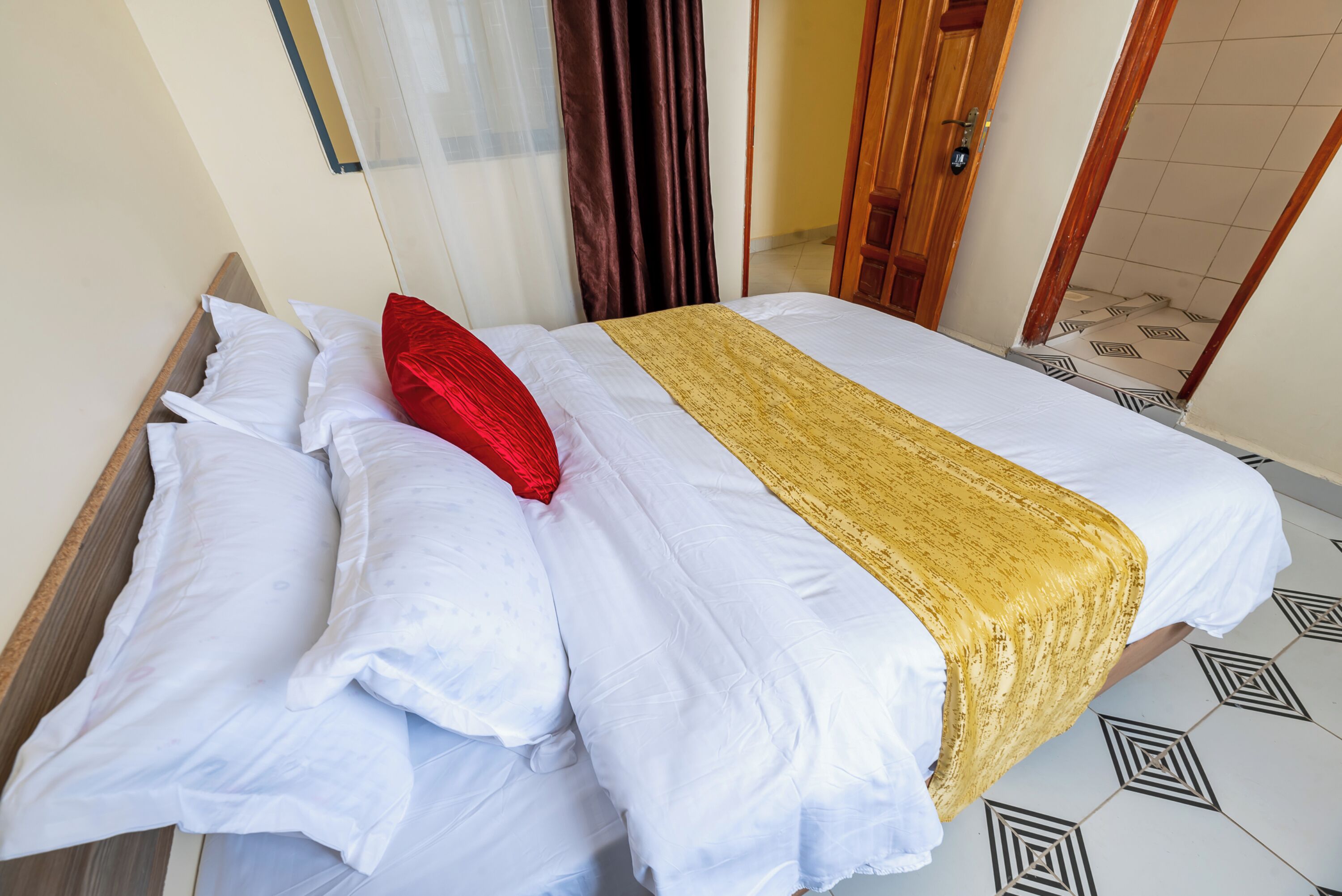 A neatly made bed with white and red pillows, a gold bedspread, and a wooden headboard.