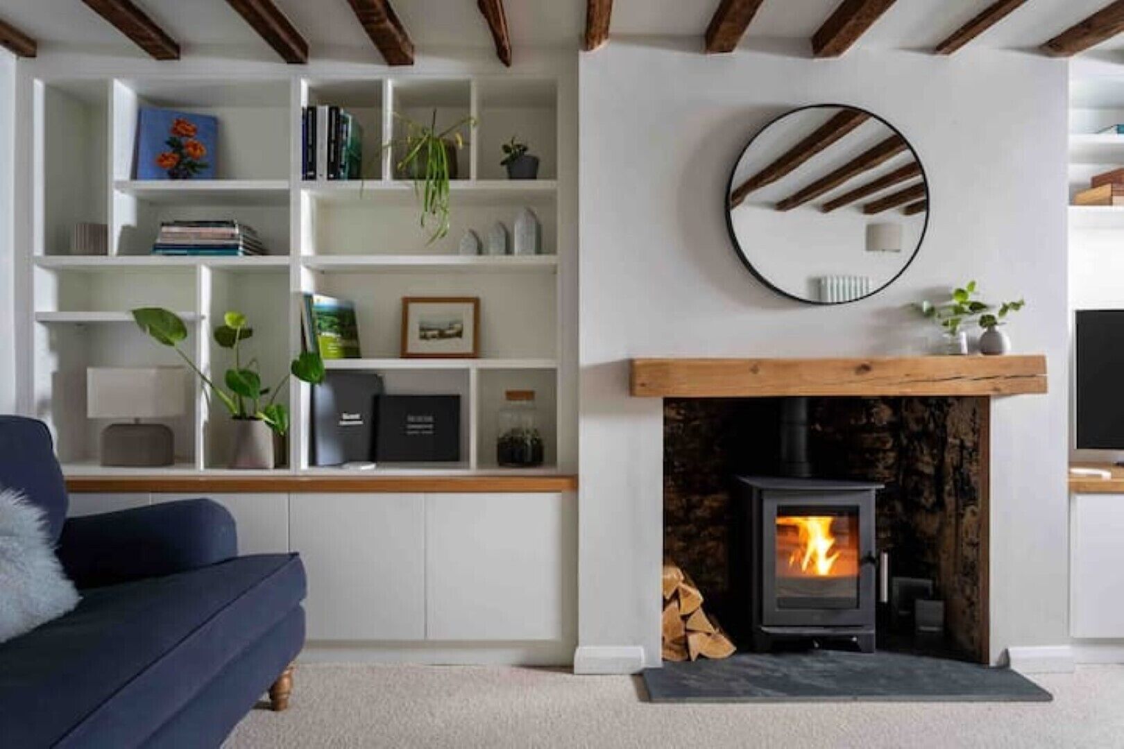 A living room with a fireplace, a blue sofa, and a white shelving unit with books and plants.