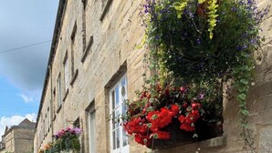 A street view of Cecily Hill with stone buildings, flower boxes, and a clear sky.