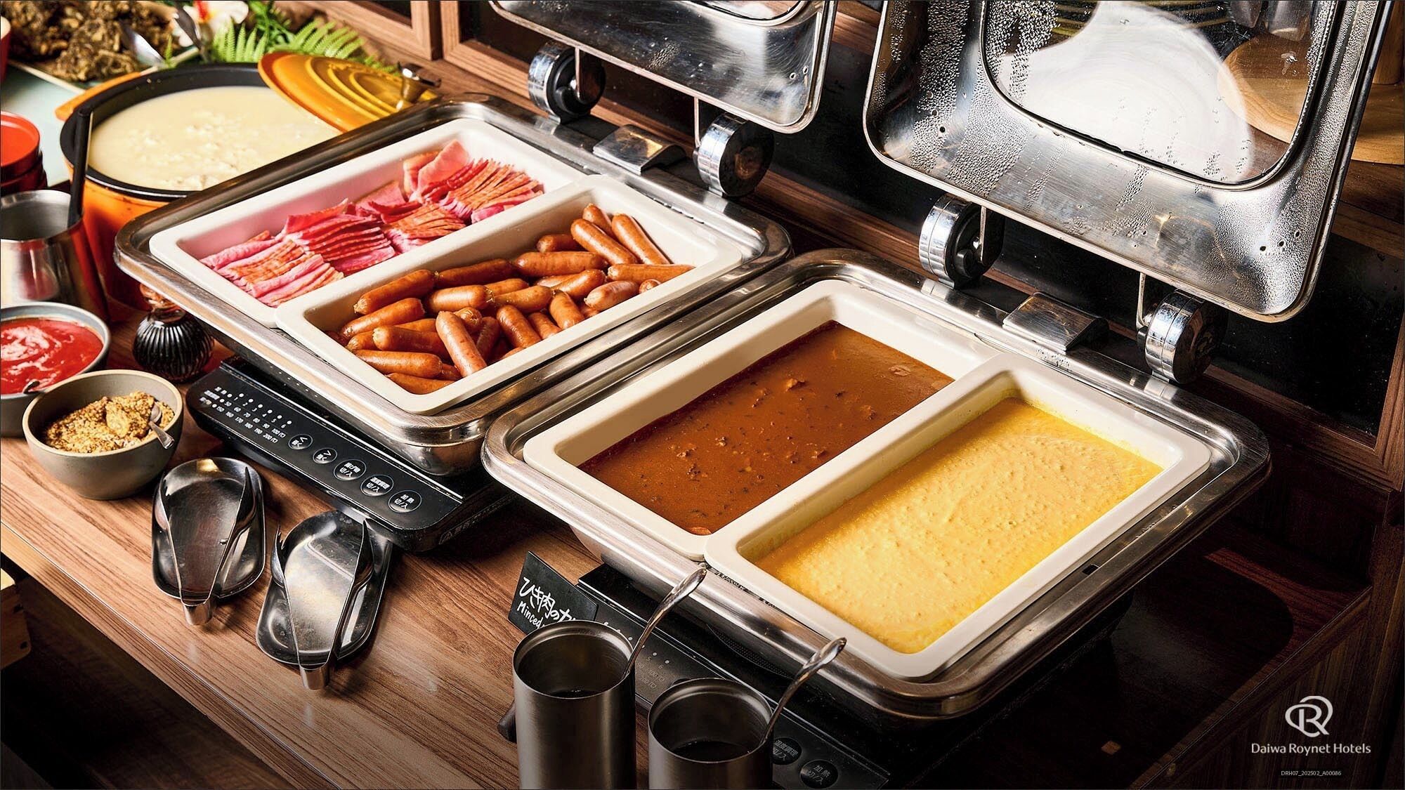 A buffet setup with various dishes including sliced meats, sausages, and a creamy soup.