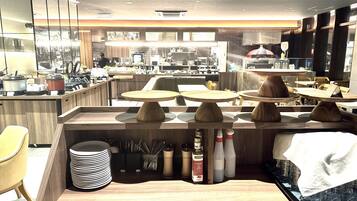 A modern restaurant interior with wooden tables, a kitchen area in the background, and various dining utensils on the counter.