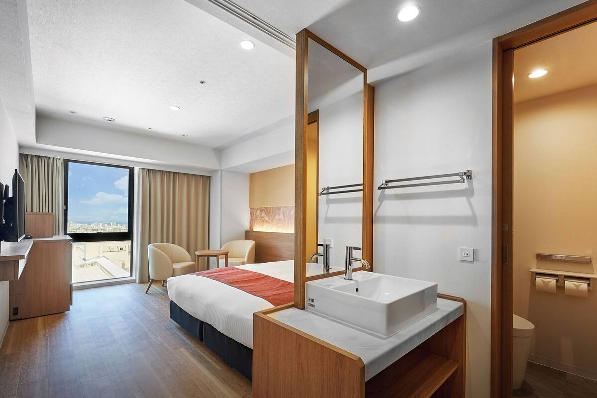 Een moderne hotelkamer met een groot bed, een badkamer met wastafel en spiegel, een bureau en uitzicht op de stad.