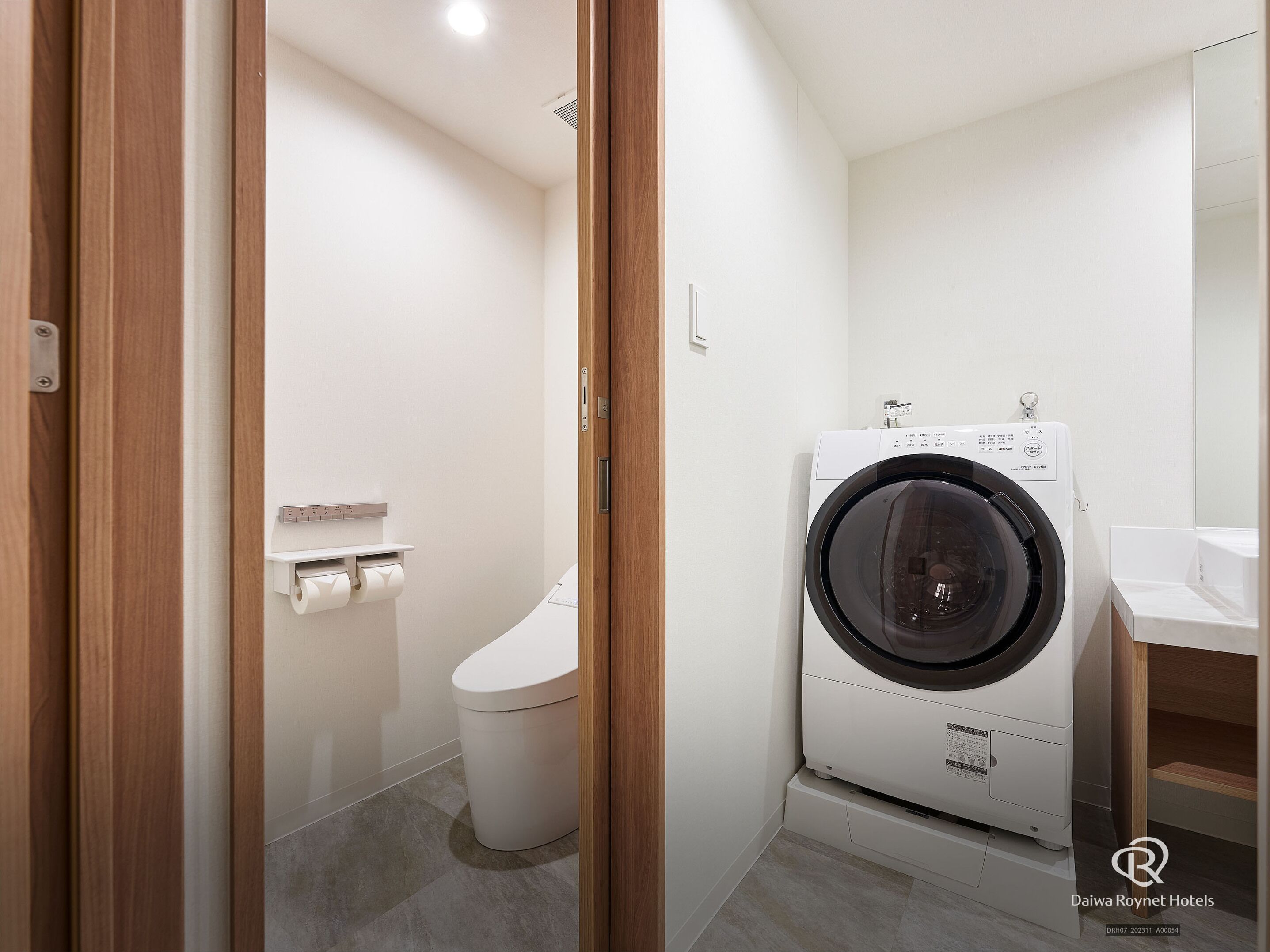 A modern bathroom with a toilet, a washing machine, and a sink.