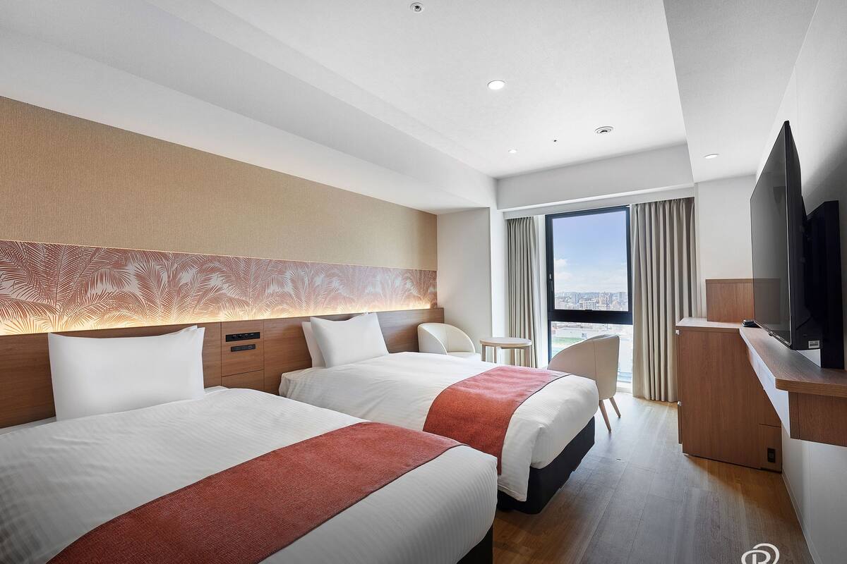 Een hotelkamer met twee bedden, een televisie, een bureau en uitzicht op de stad.