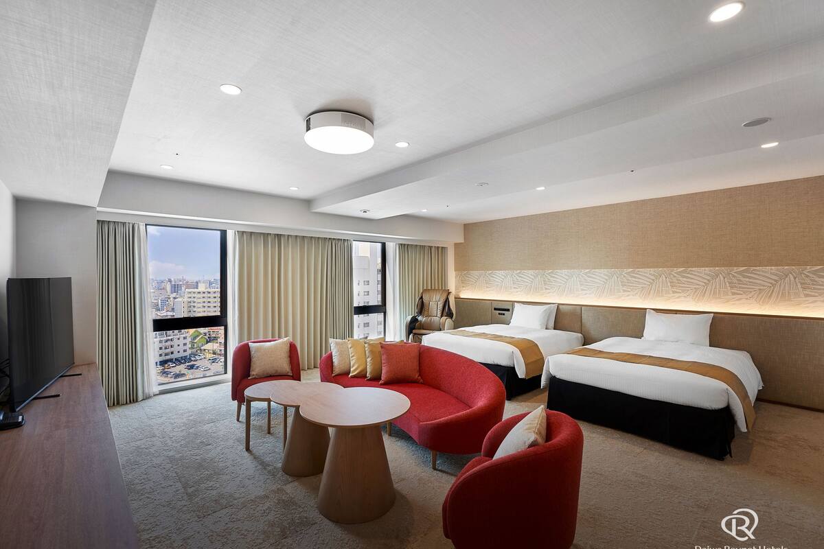 Een hotelkamer met een groot bed, twee kleinere bedden, een sofa, een televisie en uitzicht op de stad.