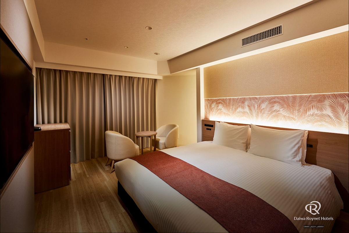 Een hotelkamer met een bed, een bureau, een stoel en een raam met gordijnen.