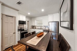 A modern kitchen with white cabinetry, stainless steel appliances, and a wooden dining table.