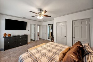 A bedroom with a bed, dresser, TV, ceiling fan, and doors leading to other rooms.