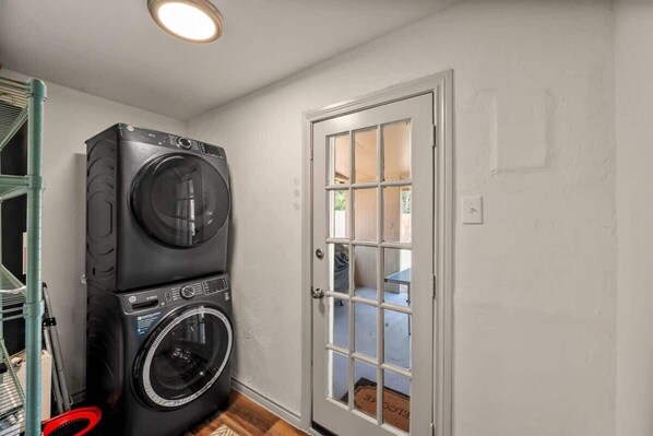 Lavandería con lavadoras y secadoras apiladas, una puerta que da a un espacio exterior y un interruptor de luz visible en la pared.