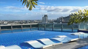 A rooftop infinity pool with clear blue tiles, a glass railing, and a cityscape view in the background.