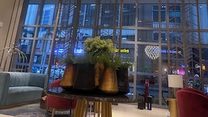 A modern lobby with a large spherical chandelier, a seating area with a blue sofa, and a view of a cityscape through large windows.