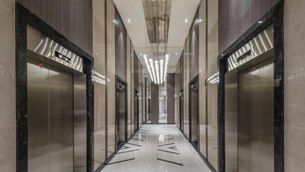 A modern hallway with elevators, marble floors, and glass doors.