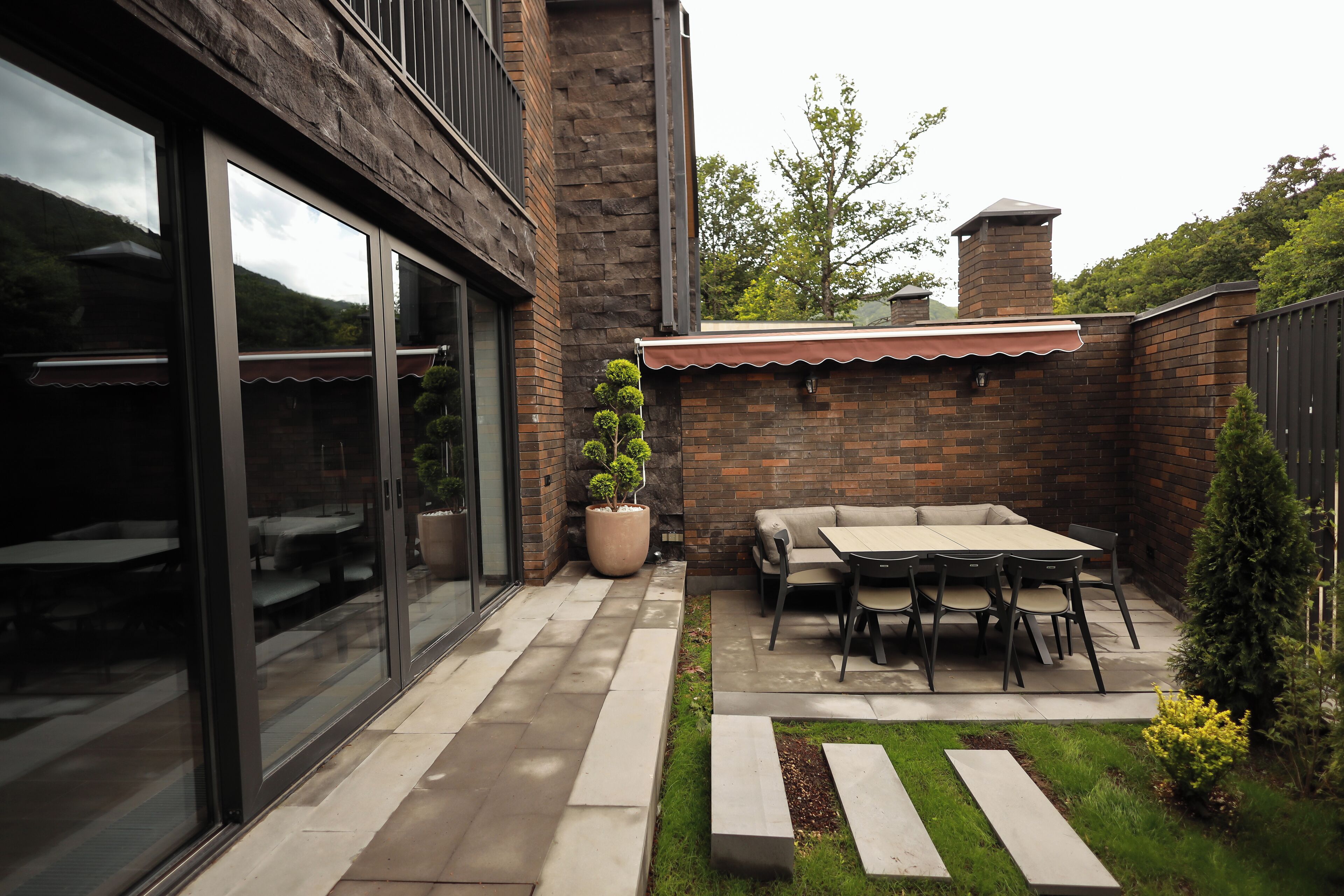 A patio with a table and chairs, a potted plant, and a brick wall.