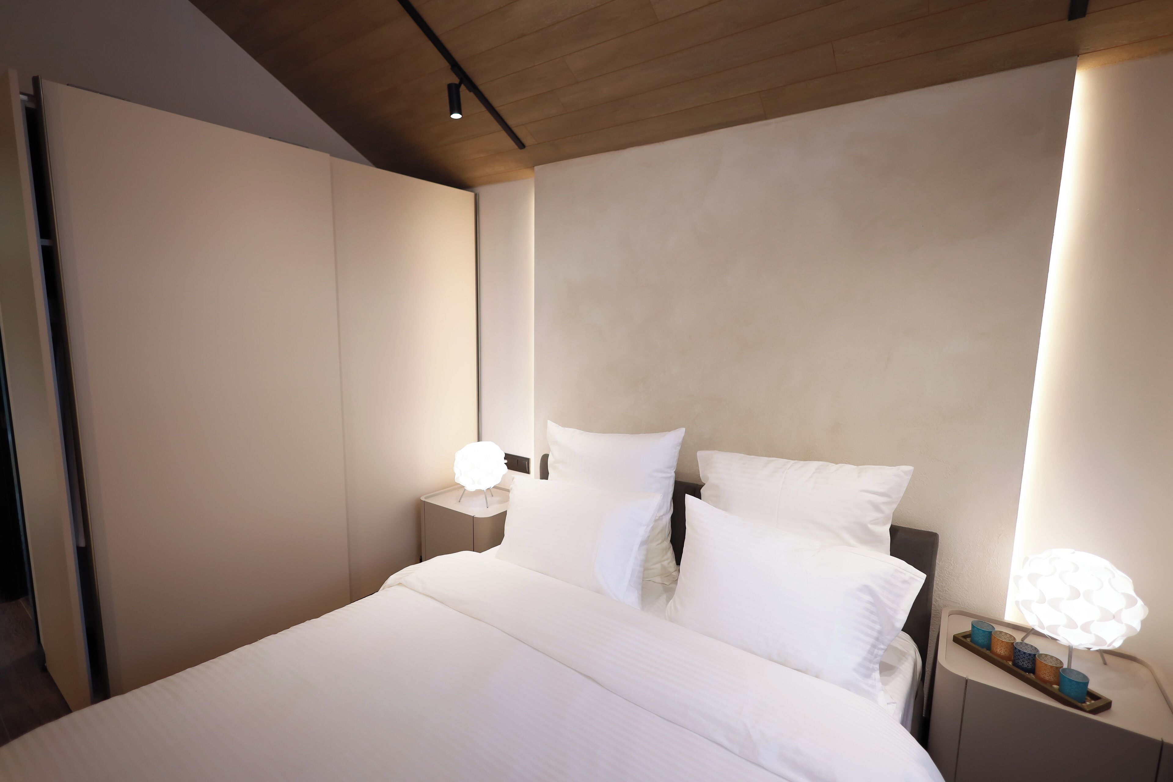 A modern hotel room with a large bed, two bedside tables with lamps, and a wardrobe.