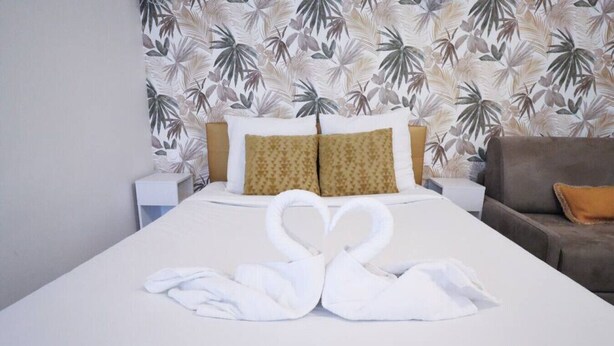 Une chambre d’hôtel avec un lit bien fait, un canapé marron et un papier peint à motifs.