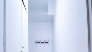 Un couloir étroit aux murs blancs et au plancher en bois. Il y a deux portes sur le côté gauche et un porte-manteau avec trois crochets au centre.