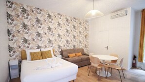 Une chambre d’hôtel comprenant un lit, un canapé, une table à manger avec des chaises, un luminaire suspendu et une porte.