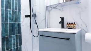 Une salle de bain avec une douche à parois de verre, un lavabo en marbre blanc et un miroir au-dessus.