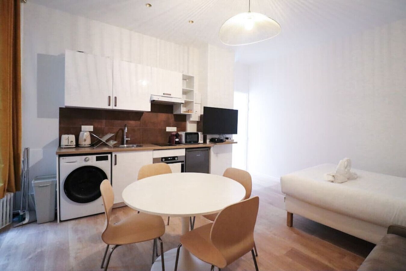 A compact kitchen with modern appliances, a dining table with chairs, and a sofa.