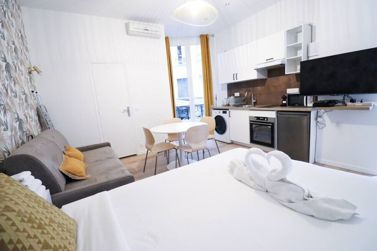 Een compacte hotelkamer met een bed, een eettafeltje, een slaapbank, een wasmachine en een kitchenette.