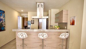 Una cocina moderna con una isla central, tres taburetes blancos de bar, electrodomésticos de acero inoxidable y un dispensador de agua.