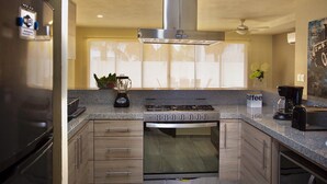 Una cocina moderna con estufa de acero inoxidable, horno empotrado, licuadora y estación de café.
