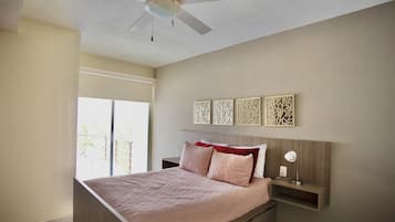 A bedroom with a bed, a ceiling fan, a window, and wall art.