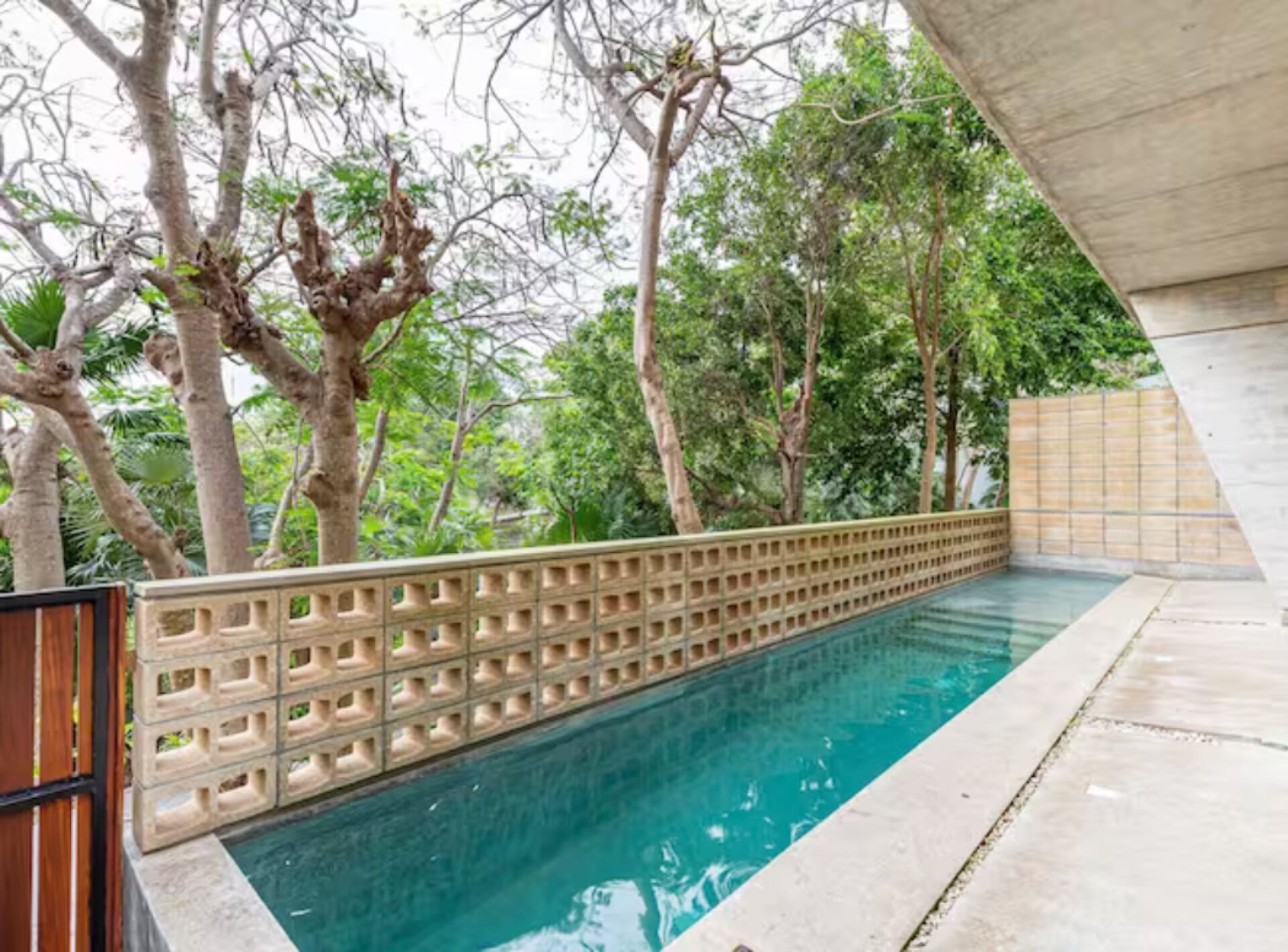 Une piscine entourée d’une clôture en bois, bordée d’arbres et d’une structure en béton.