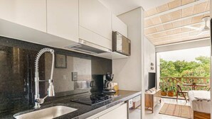 A modern kitchen with a black countertop, stainless steel sink, and a built-in stove. There is a wooden deck visible through an open door. - Incredible Loft With Pool (Cancún)
