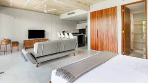 A modern bedroom with a large bed, a grey sofa, a TV, and a wooden wardrobe. - Fresh Large Loft With Pool (Cancún)