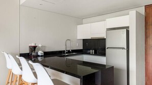 A modern kitchen with a central island, white bar stools, a coffee machine, and a refrigerator. - Fresh Large Loft With Pool (Cancún)