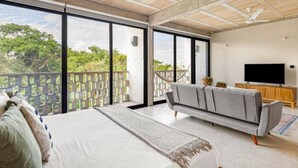 A spacious room with a large bed, a grey sofa, a TV, and a balcony with a view of greenery. - Latest Large Loft With Pool (Cancún)