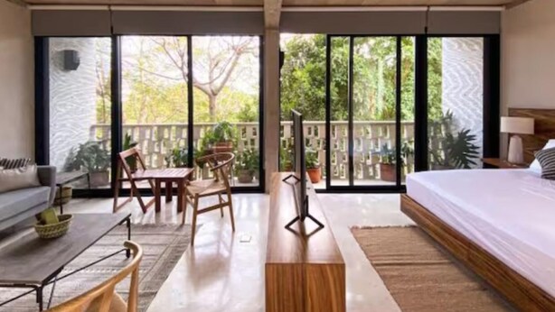 A modern hotel room with a large bed, a sofa, a dining table with chairs, and a balcony with potted plants. - Stylish - Large Loft With Pool (Cancún)