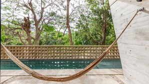 A hammock by a pool with a wooden fence and trees in the background. - Stylish - Large Loft With Pool (Cancún)