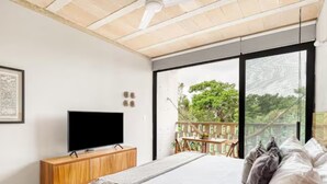 A bedroom with a large bed, a TV on a wooden cabinet, and a balcony with a view of trees. - Fabulous Loft With Pool (Cancún)