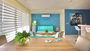 Un salon moderne avec un canapé de couleur turquoise, une table basse en bois et un coin repas agrémenté d’une plante et d’assiettes pour enfants.
