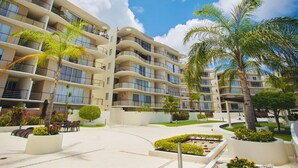 Un hôtel à plusieurs étages doté de balcons, de palmiers et d’une cour aménagée.