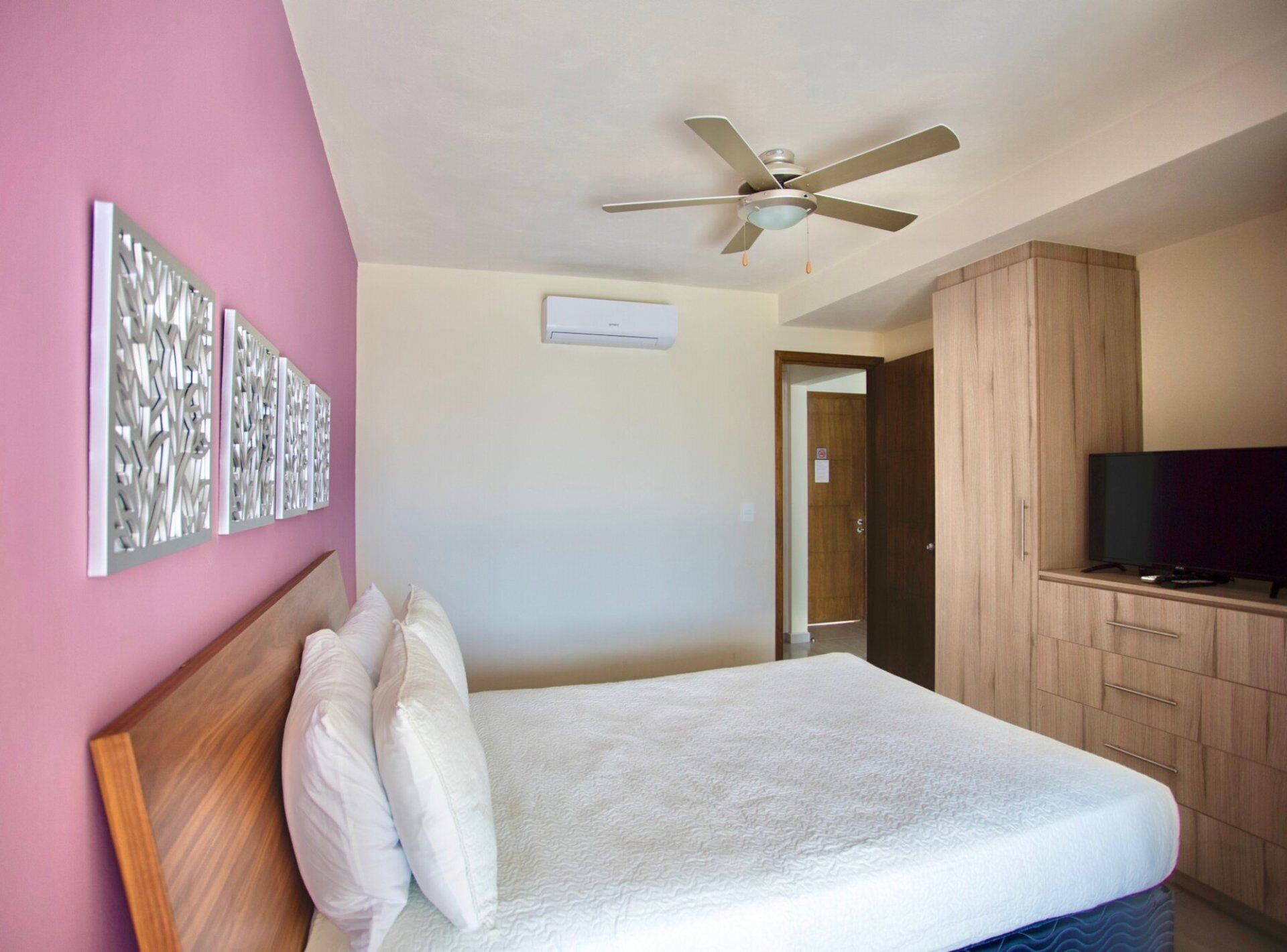 Une chambre d’hôtel avec un lit, un ventilateur de plafond, une télévision et une armoire en bois.