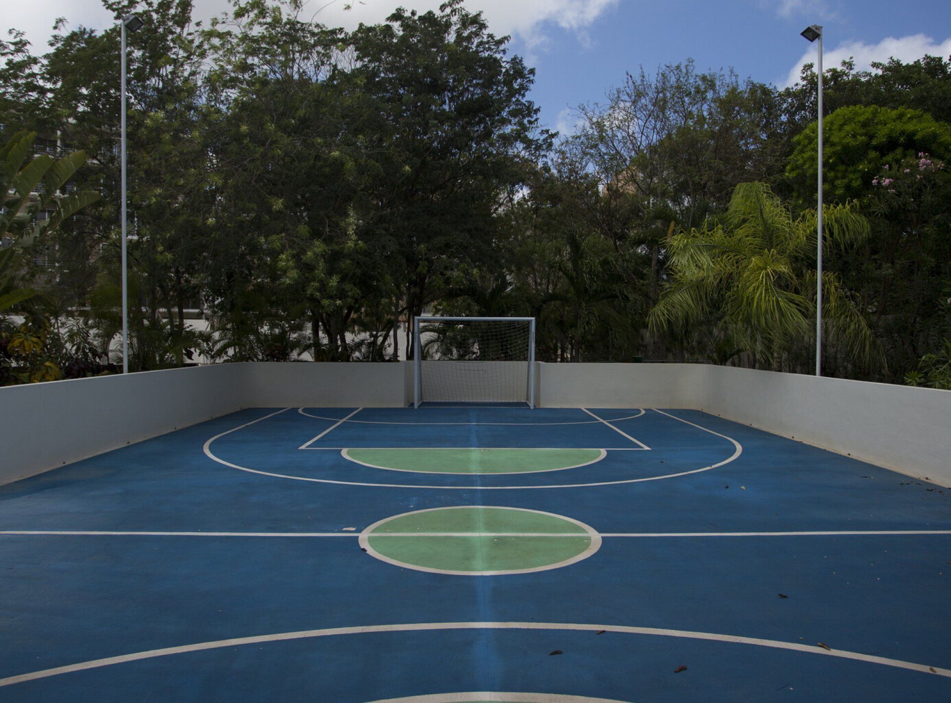 An outdoor basketball court with a goal post, surrounded by trees and a clear sky.