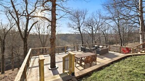 Eine Holzterrasse mit Gartenmöbeln, umgeben von Bäumen und Blick auf die Landschaft.