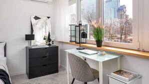 Un dormitorio moderno con escritorio, una silla, cómoda y un amplio ventanal con vistas a la ciudad.